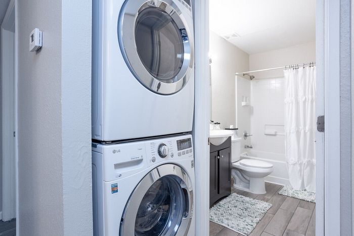 Modern apartment featuring a sleek stackable washer and dryer beside a chic, bright bathroom with elegant fixtures.