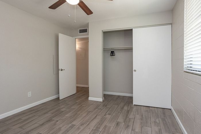 Bright, modern bedroom with sleek gray wood flooring, ceiling fan, and ample closet space, perfect for stylish living.