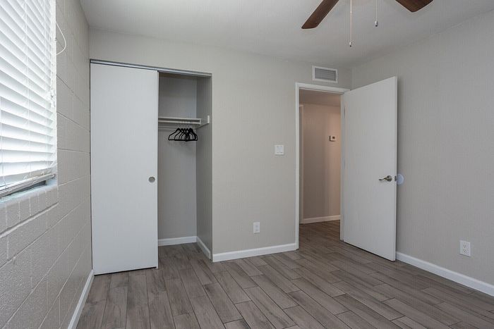 Bright bedroom with sleek wood flooring, spacious closet, and modern ceiling fan, creating a welcoming space for comfort and style.