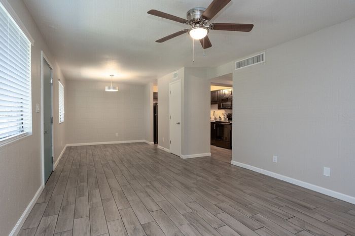 Modern open-concept living space with sleek wooden flooring, ceiling fan, and adjacent kitchen in elegant neutral tones.