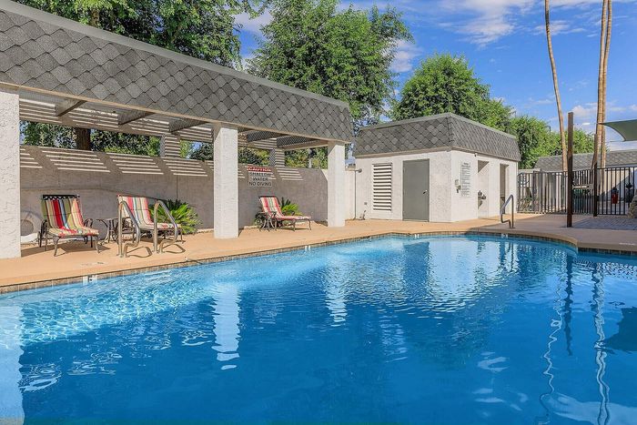 Inviting outdoor pool area featuring comfortable lounge chairs, shaded pergola, and lush greenery, perfect for relaxation.