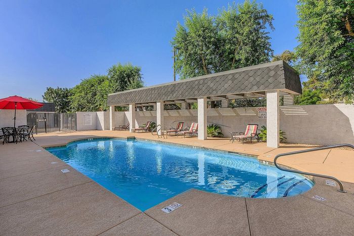 Inviting outdoor pool area with vibrant lounge chairs and a shaded pergola, perfect for relaxing under the sunny skies.