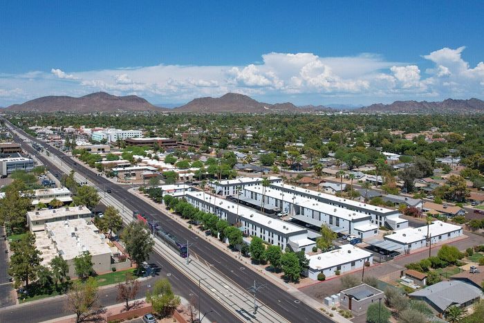 Aerial view of a modern apartment complex set within a vibrant urban landscape, with scenic mountain views under a clear blue sky.