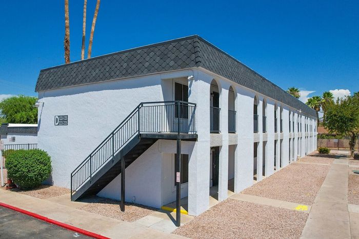 Modern apartment complex with stylish exterior featuring sleek black railings and a pristine white facade under a clear blue sky.