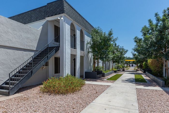 Modern apartment complex with elegant white facades, lush landscaping, and a serene pathway under a vibrant blue sky.