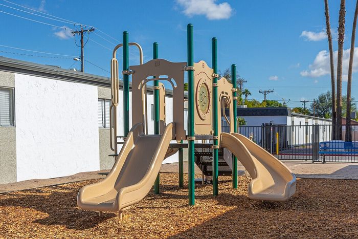Inviting playground with slides and climbing structures, set against a clear blue sky in a vibrant apartment community.