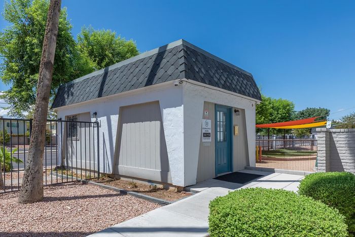 Charming office building with a quaint blue door, surrounded by lush greenery and vibrant outdoor spaces under clear blue skies.