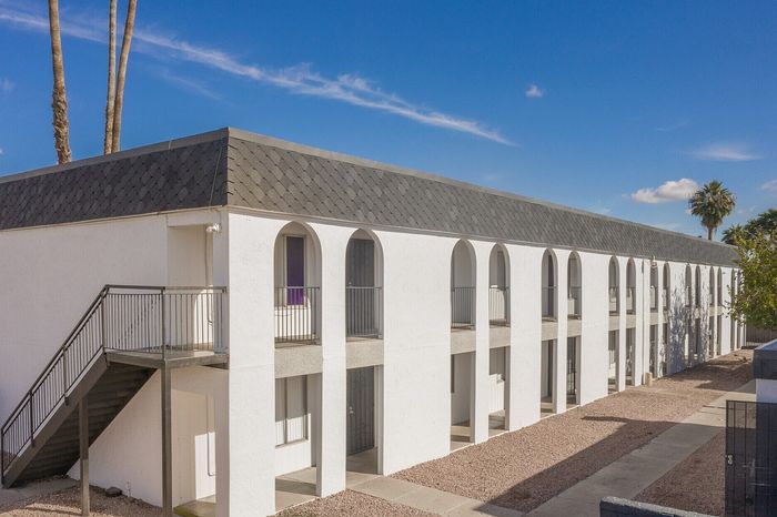 Modern two-story apartment building with arched balconies and a sleek exterior, set against a clear blue sky.