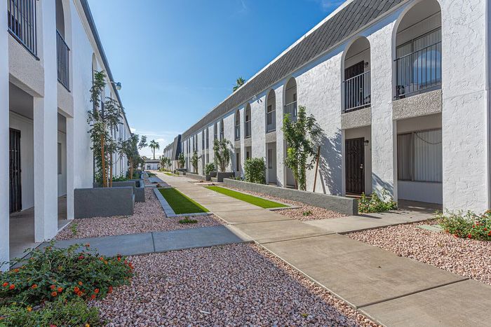 Modern apartment complex with stylish white arches, lush landscaping, and a serene walkway under the clear blue sky.
