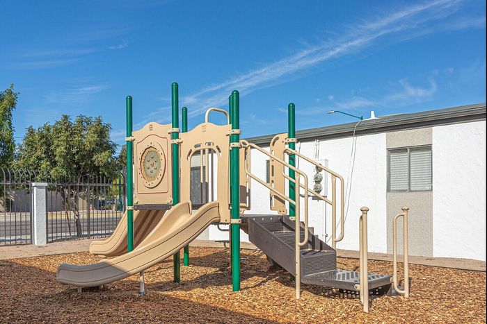 Inviting community playground with slides and climbing structures, set against a bright blue sky and surrounded by trees.