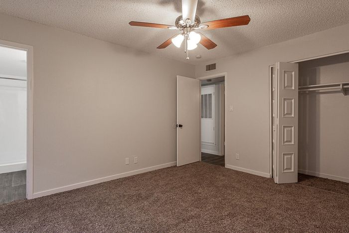 Bright bedroom featuring an elegant ceiling fan, spacious closet, and plush carpet, perfect for comfort and relaxation.