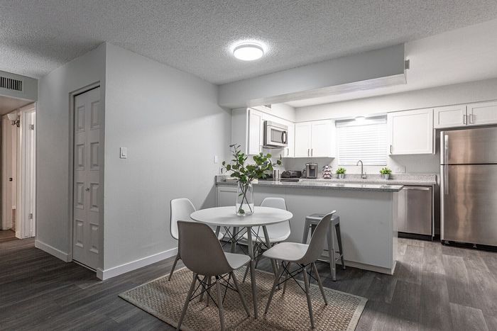 Contemporary dining area with sleek white furniture and open-plan kitchen featuring modern stainless steel appliances.