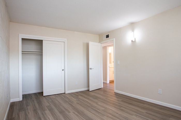 Bright and spacious room with sleek wooden flooring, a modern closet, and minimalist white walls.