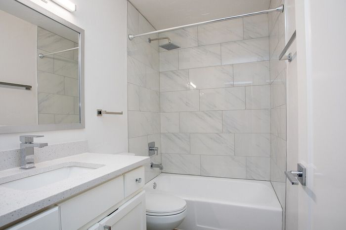 Modern bathroom with elegant white countertop, sleek vanity mirror, and chic tile shower.