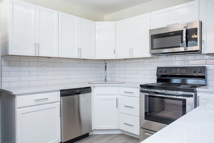 Contemporary kitchen with sleek stainless steel appliances, white cabinets, and modern subway tile backsplash.