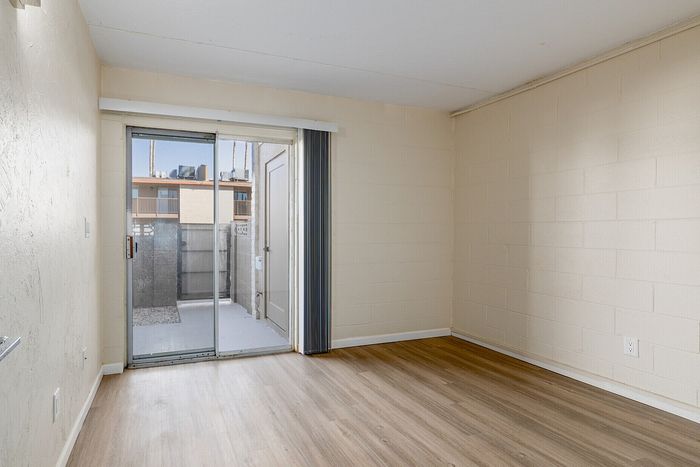 Bright and airy room with sleek wood flooring, featuring a large sliding glass door leading to a private patio area.