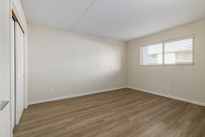 Bright and spacious room featuring elegant wood flooring and a large window with horizontal blinds, ideal for a cozy bedroom or home office.