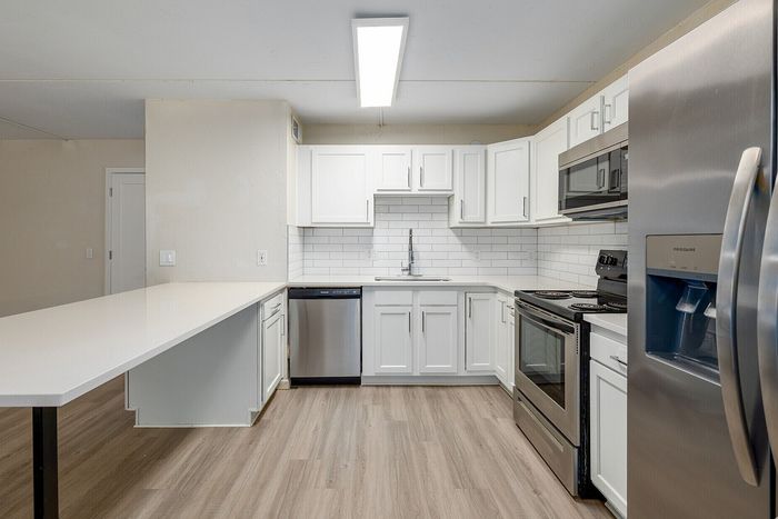 Modern apartment kitchen with sleek white cabinetry, stainless steel appliances, and a spacious countertop in a light-filled setting.
