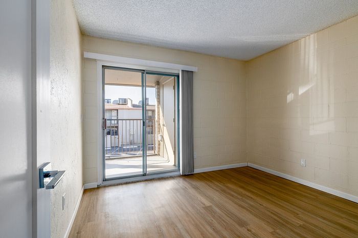 Bright room with sleek wooden flooring and sliding glass doors leading to a private balcony with city views.