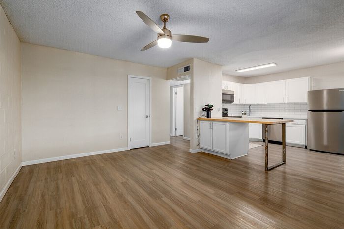 Modern open-plan living space with elegant wooden floors, featuring a sleek kitchen with stainless steel appliances and stylish white cabinetry, perfect for contemporary living.
