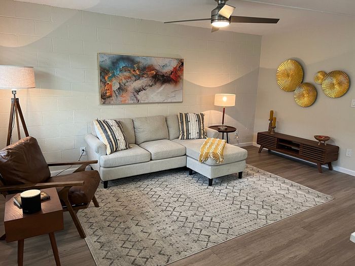 Inviting living room with a cozy beige sectional, chic modern art, and elegant gold wall decor, complemented by warm lighting and a stylish rug.