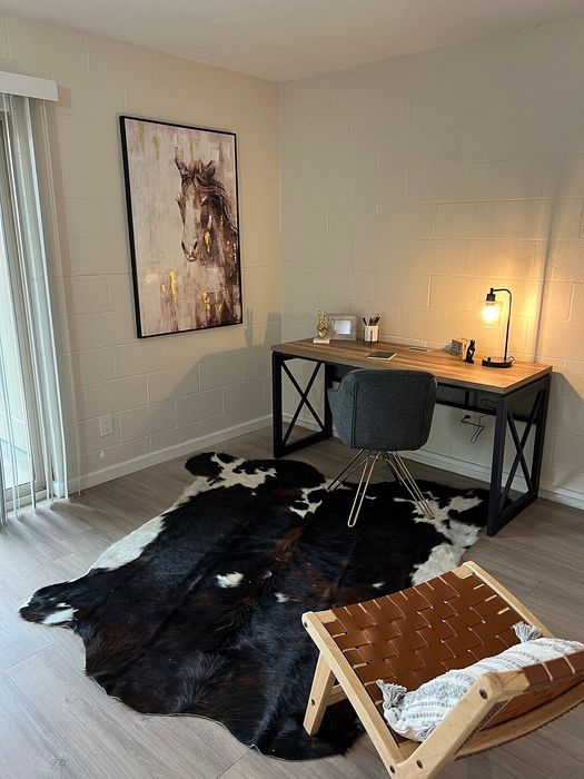 Chic home office featuring a stylish wooden desk with modern lighting, complemented by a cozy chair on a luxurious cowhide rug, and adorned with elegant horse artwork.