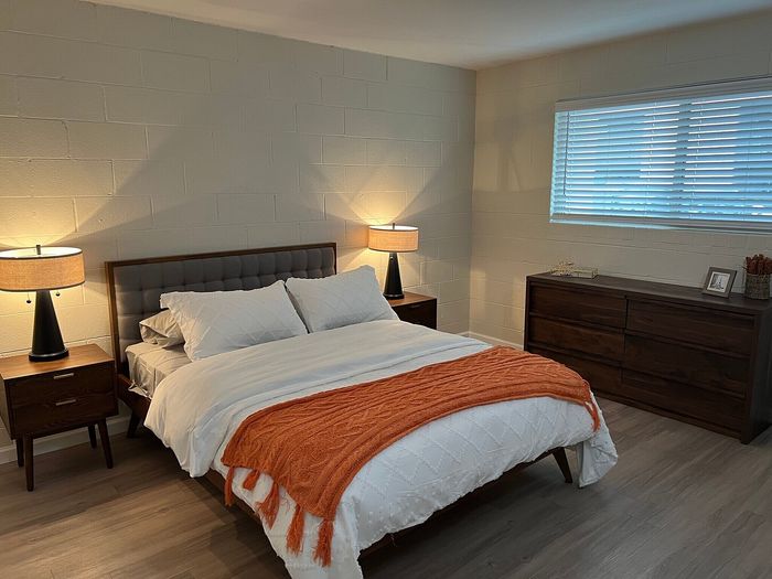Inviting bedroom with modern wooden furniture, cozy lighting, and elegant decor, featuring a comfortable bed with vibrant orange accents.