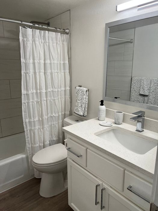 Modern bathroom featuring elegant white cabinetry, sleek vanity mirror, and contemporary fixtures with a chic shower curtain.