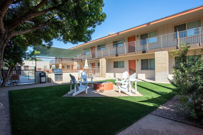 Charming apartment exterior featuring a lush courtyard with cozy seating around a stylish fire pit under shade sails, perfect for social gatherings.