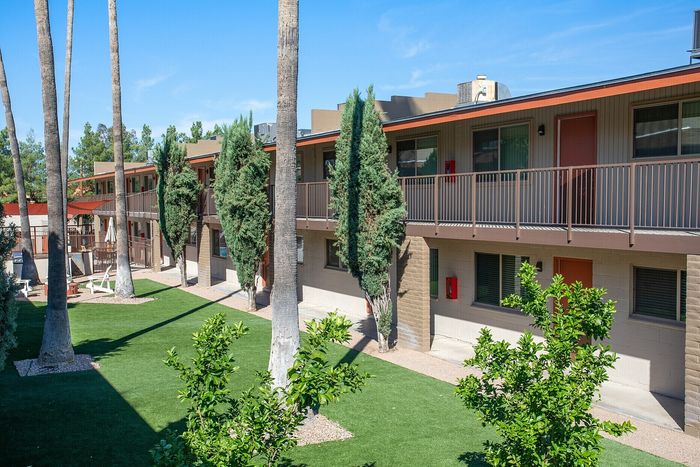 Inviting apartment complex featuring lush green landscaping, tall palm trees, and modern architecture under a clear blue sky.
