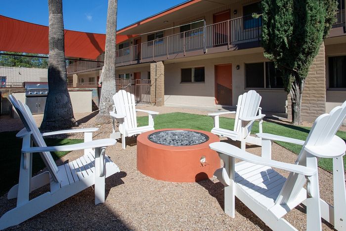 Charming apartment courtyard featuring modern Adirondack chairs around a cozy fire pit with vibrant red sunshade, ideal for relaxation and social gatherings.