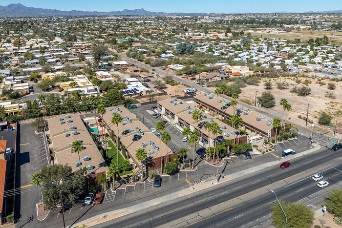 Vibrant aerial view of a sprawling apartment complex surrounded by lush palm trees and a scenic mountain backdrop, offering an ideal blend of urban convenience and natural beauty.