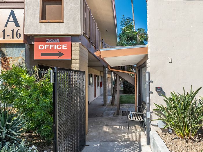 Inviting entrance to an apartment complex with modern design, lush greenery, and welcoming office sign.