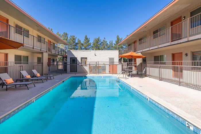 Inviting apartment complex with a crystal-clear swimming pool, surrounded by sun loungers and vibrant orange umbrellas, perfect for relaxation and enjoyment.