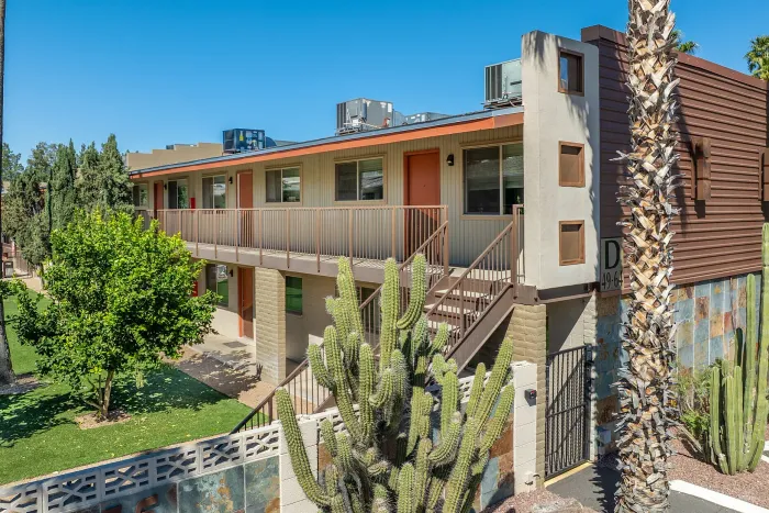 Charming apartment exterior with a modern balcony, vibrant greenery, and a lush garden, offering a serene living environment.