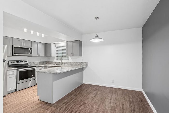 Modern kitchen and dining area featuring sleek stainless steel appliances, granite countertops, and elegant lighting in a stylish open space.