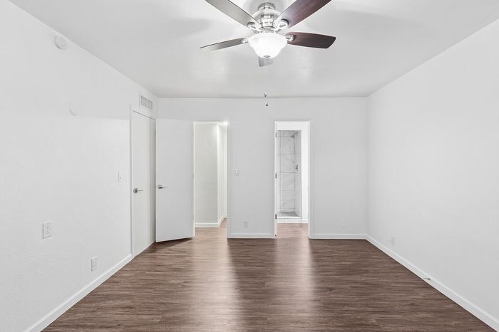 Bright and airy bedroom with elegant wood flooring and a modern ceiling fan, showcasing a sleek design leading to a stylish bathroom.
