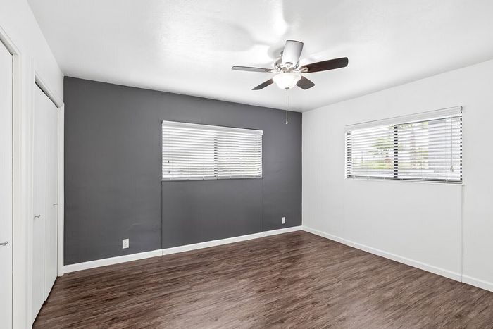 Chic, unfurnished room with elegant hardwood floors, modern ceiling fan, and abundant natural light from dual windows.