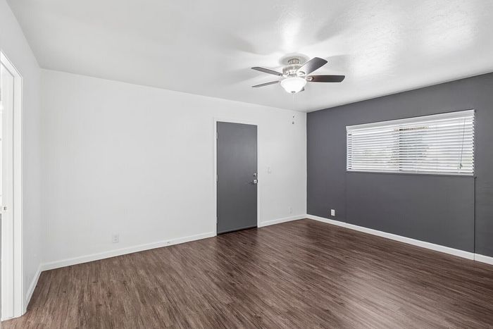 Bright and inviting room with elegant wood flooring, sleek gray accent wall, and modern ceiling fan for style and comfort.