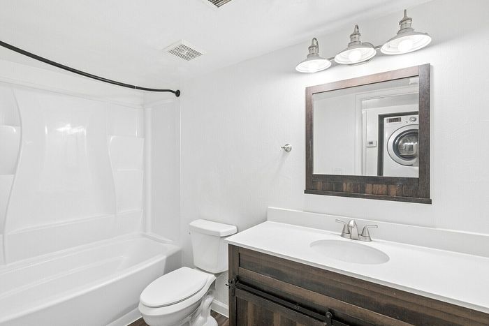 Elegant bathroom with modern white bathtub, stylish vanity with mirror, and contemporary lighting, featuring a washer and dryer conveniently located in the space.