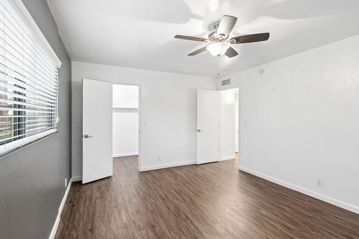 Bright and spacious bedroom with sleek hardwood floors, modern ceiling fan, and ample natural light from large windows for a cozy and comfortable atmosphere.