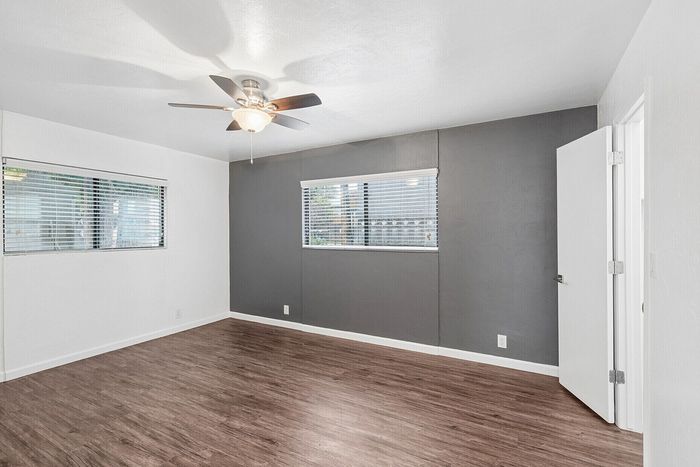 Bright and spacious room with modern wood flooring, large windows, and a stylish ceiling fan, offering a cozy atmosphere.