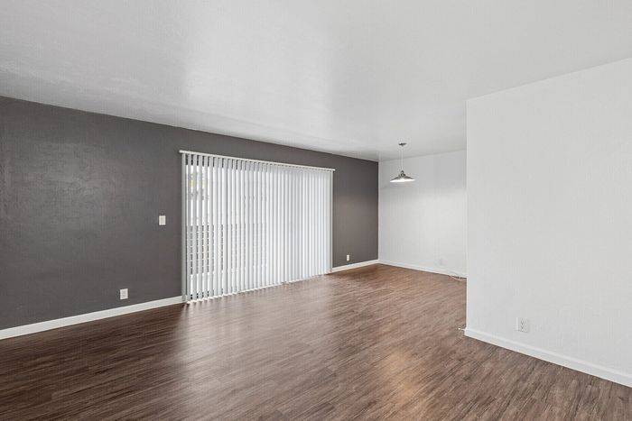 Sleek, modern living space with elegant dark wood flooring, contemporary lighting, and expansive natural light from vertical blinds.