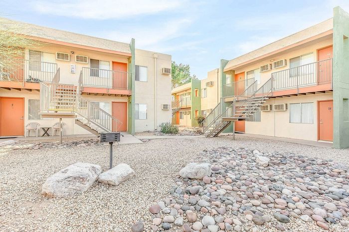 Inviting apartment complex with charming coral doors and outdoor seating, surrounded by a minimalist rock landscape under a clear sky.