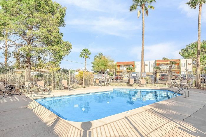 Inviting outdoor pool area with lounge chairs surrounded by lush palm trees and beautiful apartment buildings.