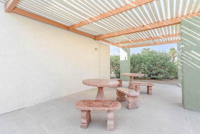 Charming outdoor patio with elegant stone tables and benches, set beneath a chic slatted pergola, offering a serene and inviting atmosphere.