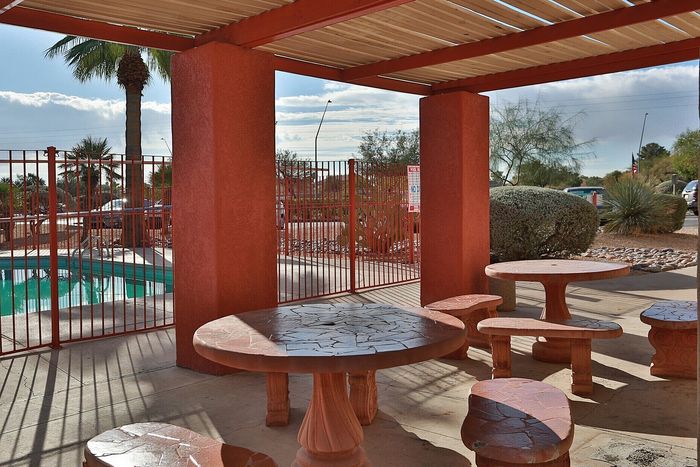 Charming outdoor patio with rustic stone tables under a pergola, adjacent to a sparkling pool and lush landscaping.