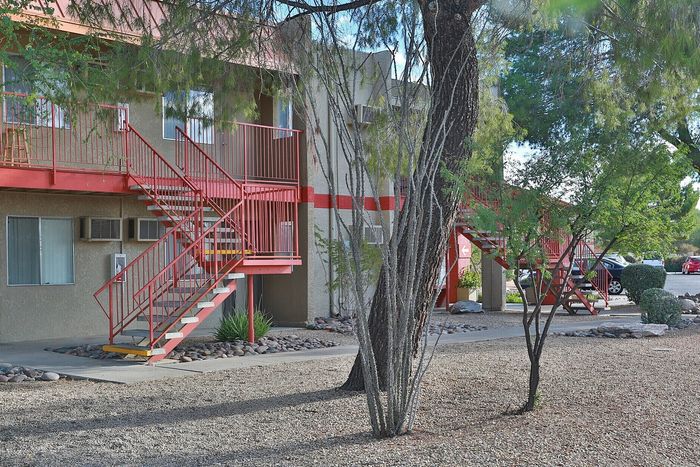 Charming apartment complex with vibrant red staircases, surrounded by lush trees and a serene landscape.