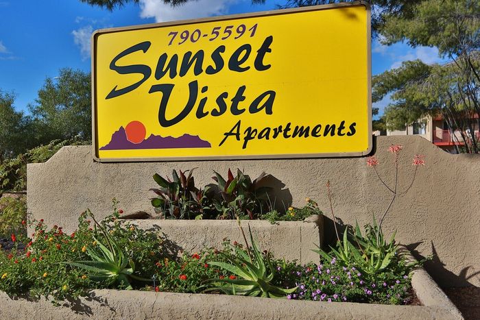 Vibrant yellow sign for Sunset Vista Apartments with lush landscaping and bright flowers showcasing inviting community living.