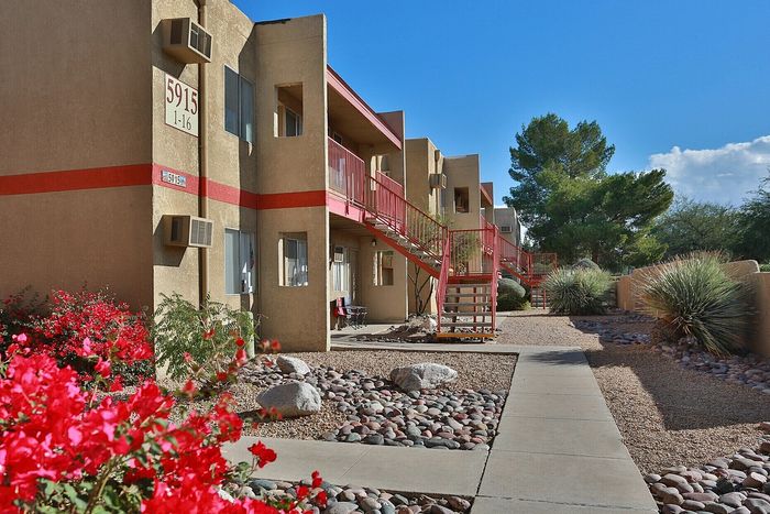 Charming apartment building with colorful desert landscaping and vibrant red staircases, set against a clear blue sky, offering modern living spaces.